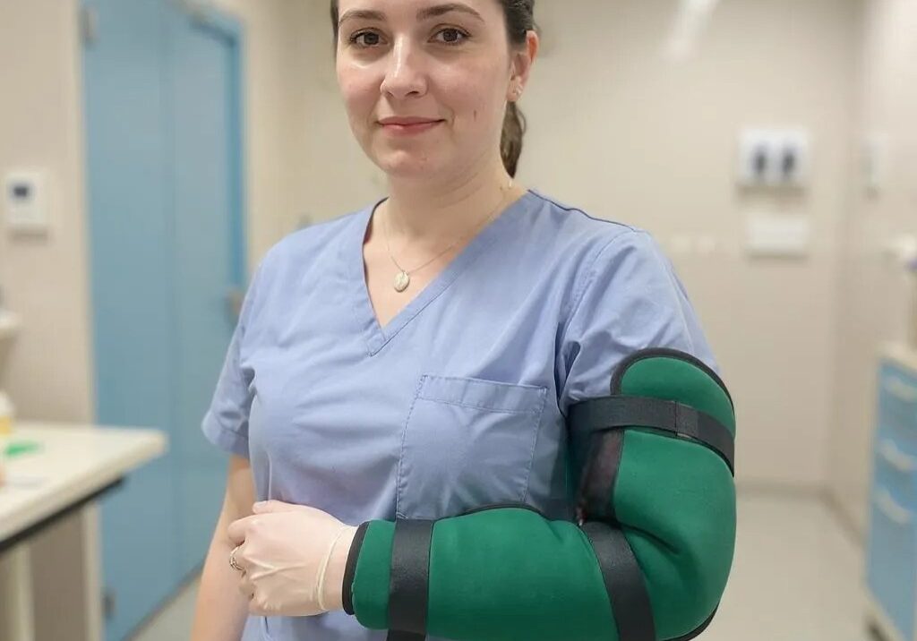 A nurse in the hospital smiling wearing the green padded upper limb protector on her arm.