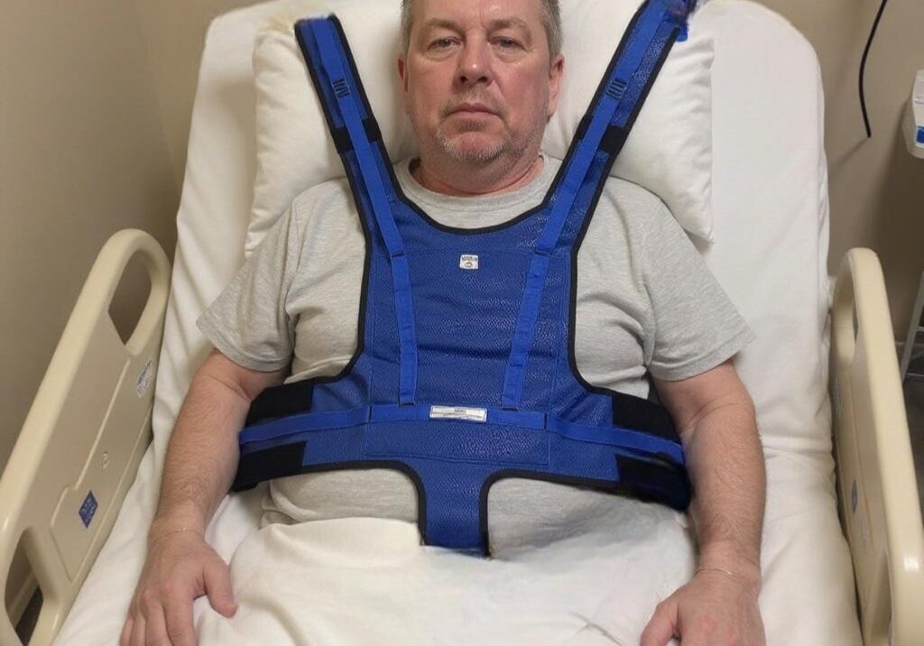 A patient in a hospital bed with the upper vest restraint attached.