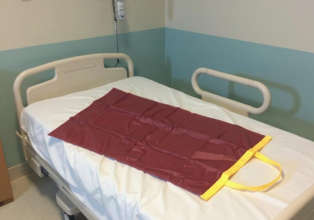 A burgundy slide sheet with yellow handles placed on a hospital bed.