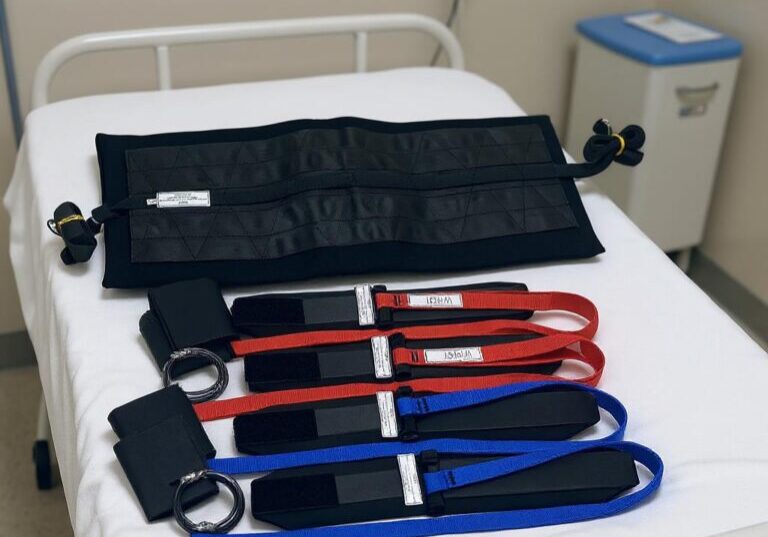 A bariatric restraint set with black cuffs and a black Toso belt placed on a hospital bed.