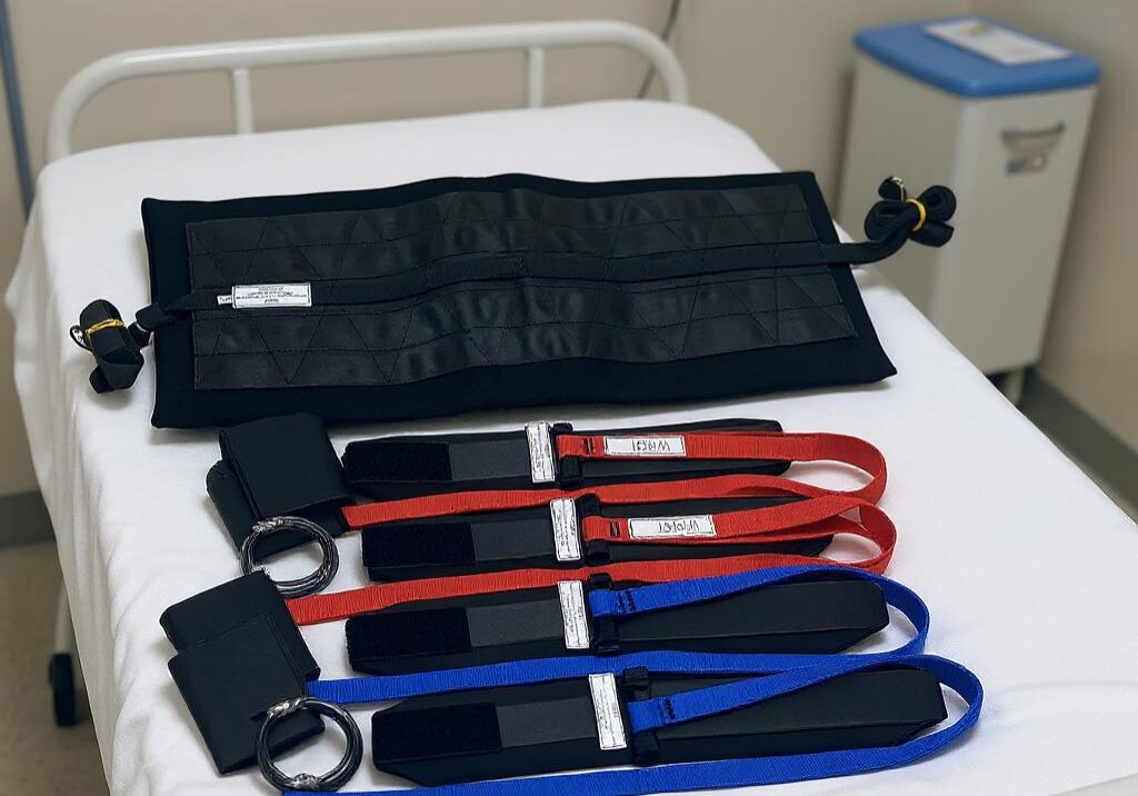 A bariatric restraint set with black cuffs and a black Toso belt placed on a hospital bed.