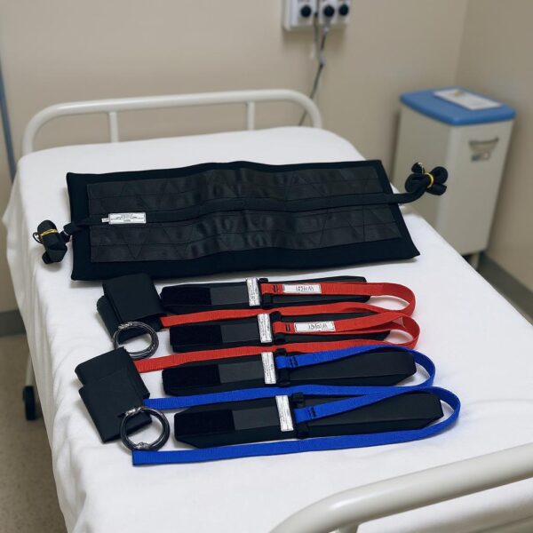 A bariatric restraint set with black cuffs and a black Toso belt placed on a hospital bed.